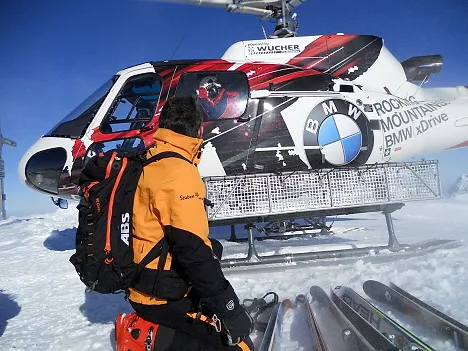 Hubschrauber im Schnee, davor ein Skifahrer mit Rucksack