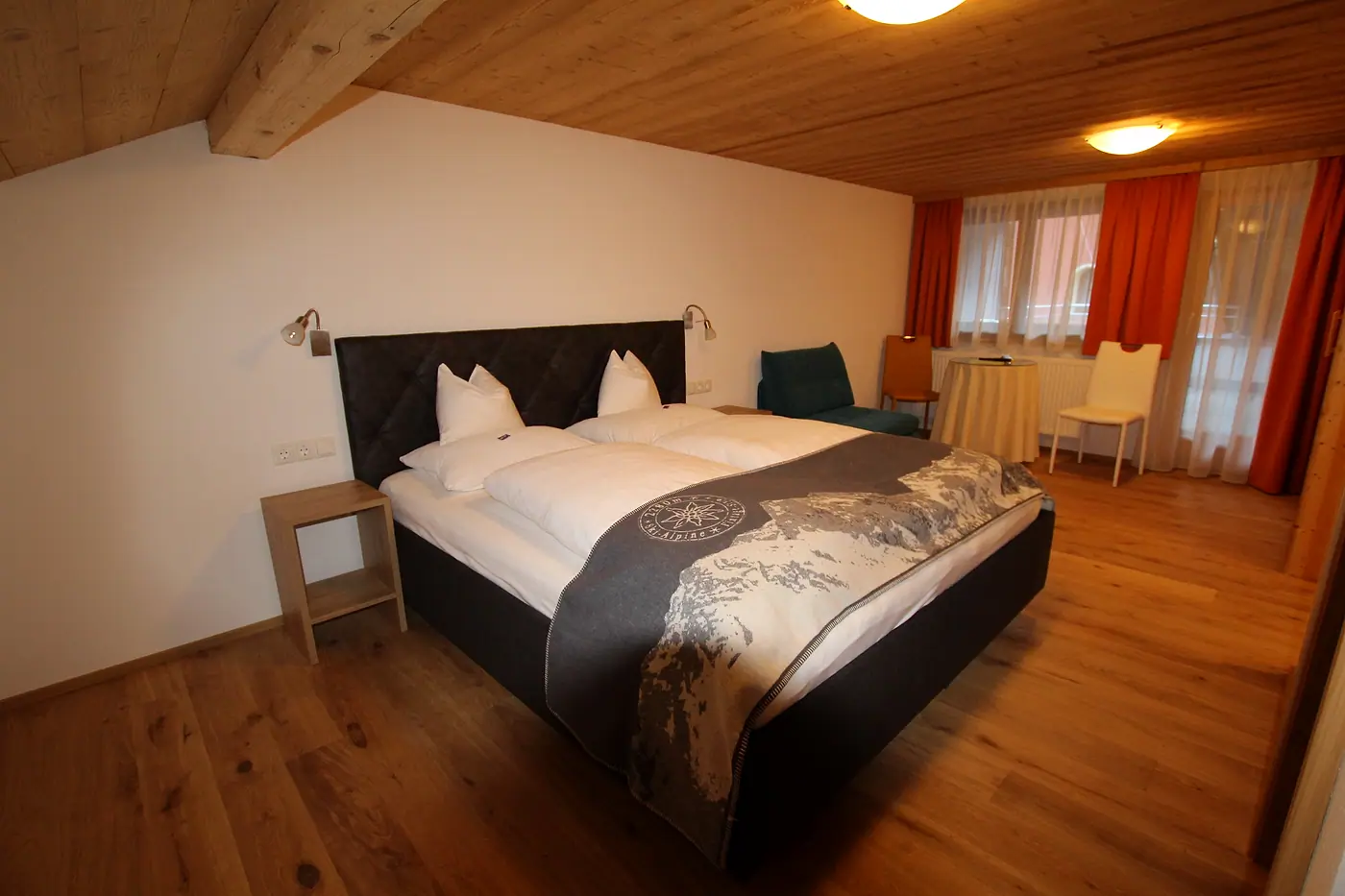 Doppelzimmer mit Holzdecke, hellem Boden und rot-weißen Vorhängen